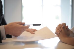 mężczyzna podaje kartkę i długopis kobiecie która ma złożone ręce